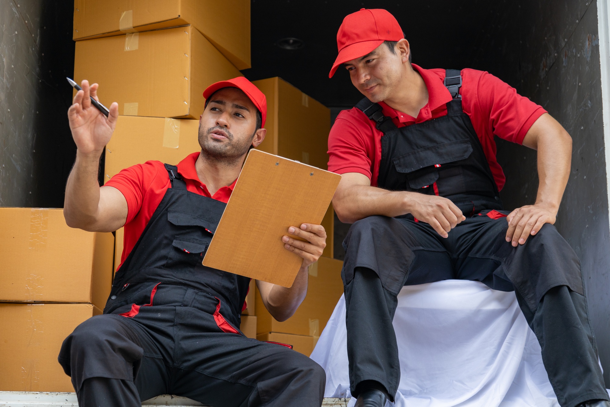 Portrait of two movers unloading boxes and furniture from a pickup truck.